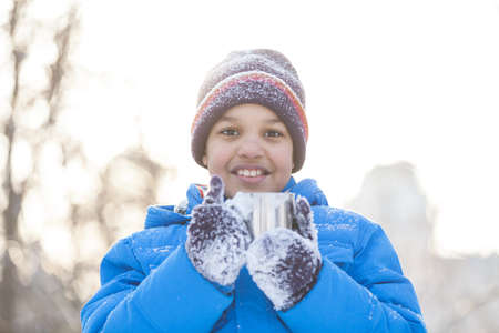 boy holding cup of hot tea. boy wearing winter blue jacketの写真素材