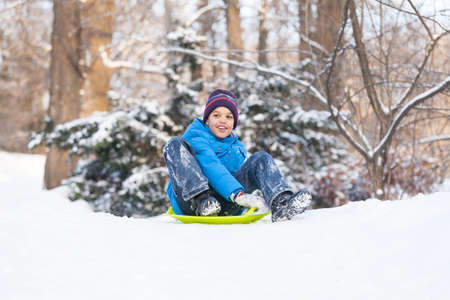 boy sitting on sledges and sliding down. child playing in park on snow in winterの写真素材