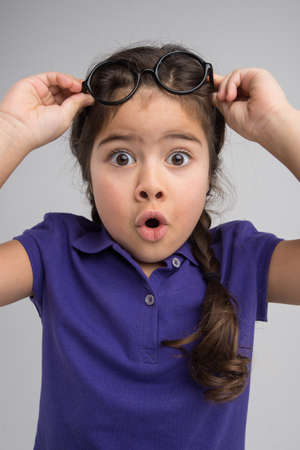 nice little girl holding glasses. pretty child removing glasses with surpriseの写真素材