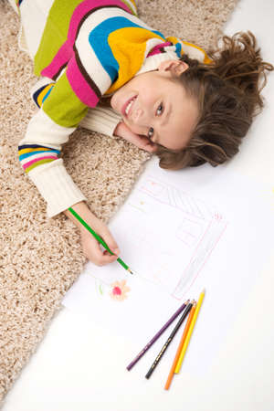schoolgirl lying on carpet and drawing pictures. waist-up and top view of little girl smilingの写真素材