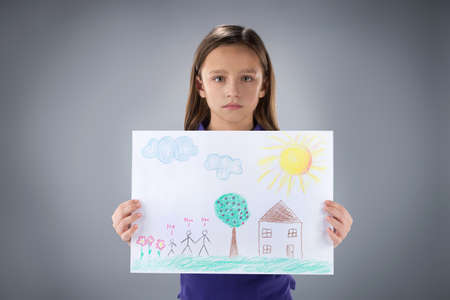 sad little girl holding picture. cute kid standing on grey background