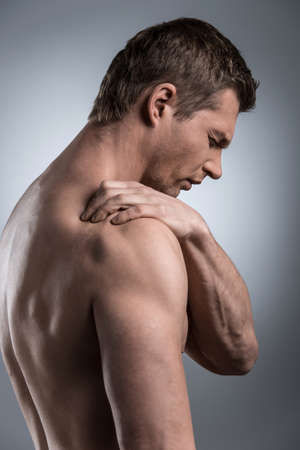 Close-up of young shirtless man with shoulder pain. young man standing on grey white background