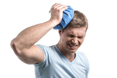 closeup of man holding icepack on his head. young man experiencing pain on white backgroundの写真素材