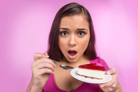 young woman hold delicious piece of cake. Brunette girl standing on pink backgroundの写真素材