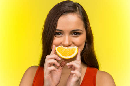 Portrait of beautiful woman holding fresh orange. front view of girl holding orange over her mouthの写真素材