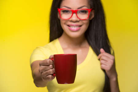 Closeup portrait of young happy woman. student wearing red glasses, giving cupの写真素材