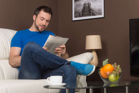 Man sitting on sofa relaxed and smiling. guy reading magazine, wearing casual clothes. の写真素材