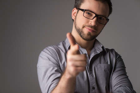 Close-up portrait of attractive young man showing gun sign. Man standing on gray background with glassesの写真素材