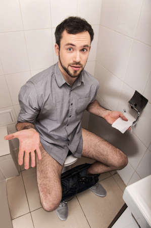 Close-up of man in toilet holding tissue. Adult man sitting on bathroom or wc toilet