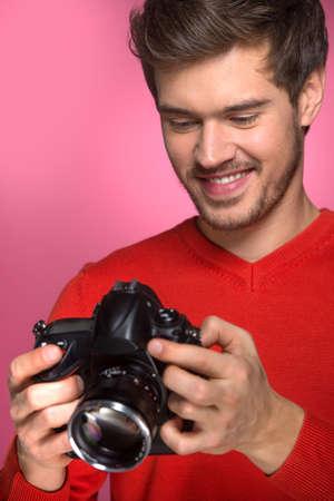 Portrait of young male with professional digital camera. man looking at camera over red background. 