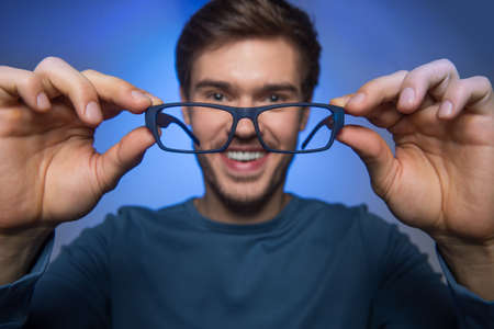 man wearing glasses to improve vision. handsome guy holding glasses on blue background.の写真素材