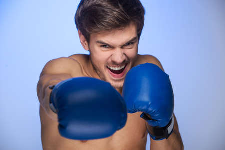 Handsome muscular young man wearing boxing gloves. Boxing man ready to fight on blue backgroundの写真素材