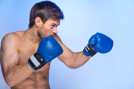 Handsome muscular young man wearing boxing gloves. Profile of man ready to fight on blue backgroundの写真素材