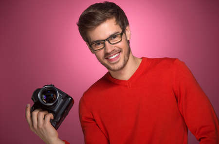 Portrait of young male with professional digital camera. man in glasses standing over red background. の写真素材