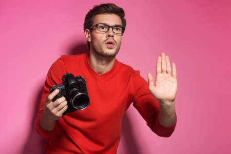 Portrait of young male with professional digital camera. man in glasses standing over pink background and gesturingの写真素材