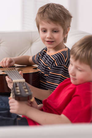 Smiling caucasian boy playing acoustic guitar. boys sitting on couch and adjusting stringsの写真素材