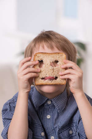 portrait of funny boy playing with bread. boy holding bread with holes and showing tongueの写真素材