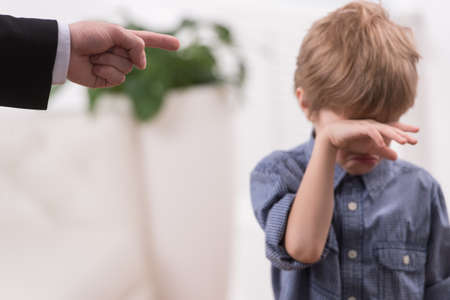 Strict father discipline naughty son. Isolated on white background boy wiping tearsの写真素材