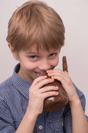 Child licks chocolate glaze from jar. nice boy holding jar and eating chocolateの写真素材