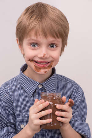 Smiling kid eating chocolate from jar. Smeared stained with chocolate lips on whiteの写真素材