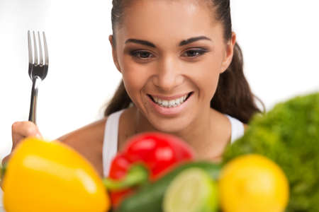 Girl with vegetables isolated on white background. happy young woman looking at vegatables and holding forkの写真素材