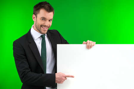 Happy smiling business man showing blank signboard. Young guy standing isolated over green backgroundの写真素材