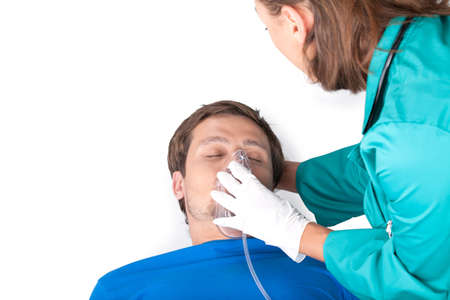 Young doctor putting oxygen mask. closeup of young man lying on white background