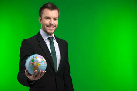 Young businessman keeps world in his hand. Smiling man holding Earth on green background の写真素材