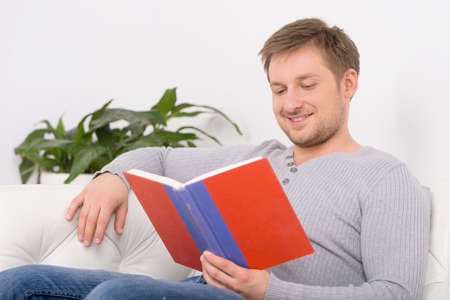 Closeup portrait of young, handsome man reading book. man reading book sitting on sofa
