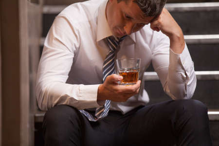 Handsome young man sitting on stairs. closeup of guy drinking whisky and thinkingの写真素材