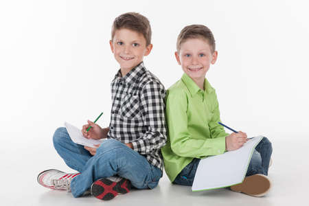 two cute boys sitting on floor drawing. cute boys using pens to draw pictures, isolated on white の写真素材