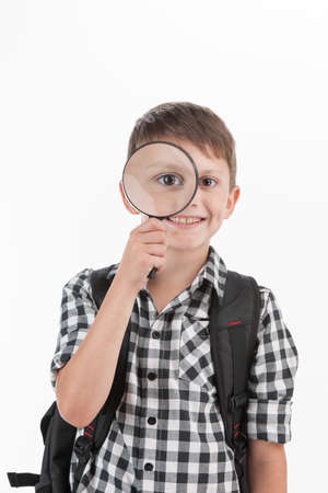 Happy schoolboy wearing backpack and holding magnifying lens. cute schoolboy walking isolated on white backgroundの写真素材