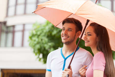 Portrait of woman and man standing under umbrella. beautiful couple walking in rain and smilingの写真素材