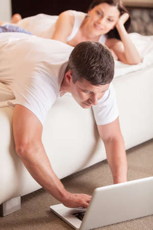 young man using computer in bed. Beatiful lovers relaxing lying on their bed の写真素材
