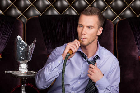Young man smoking shisha in restaurant. man resting with hookah at shisha house の写真素材