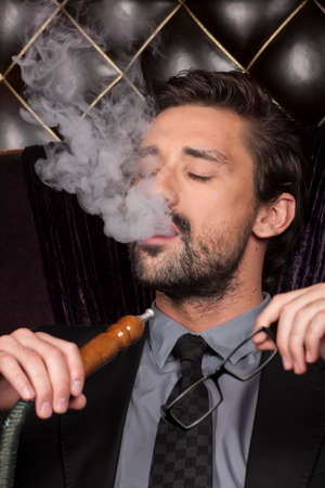 man smoking shisha at arabic restaurant. young man exhaling smoke with closed eyesの写真素材