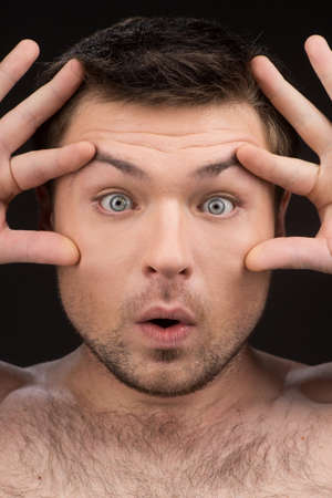 Attractive man with wide open eyes making fun. Close-up portrait of guy with eyes wide openの写真素材