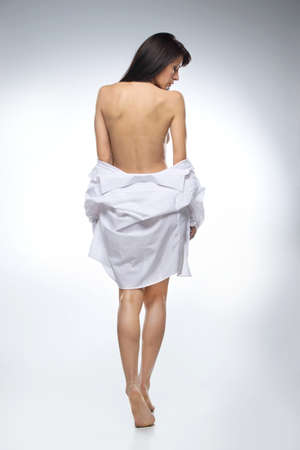 full image of beautifull woman in shirt on white background. back view of dark-haired naked girl looking downの写真素材