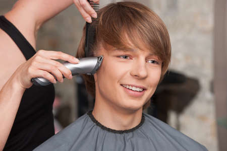 Female hairdresser cutting hair of man client using trimmer. happy man sitting in hair salon and smilingの写真素材