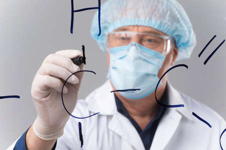 adult researcher writing formulas on transparent board. man wearing mask standing on white backgroundの写真素材