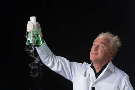 happy clinician studies in laboratory and holding flask aloft. man standing on black background and lifted flaskの写真素材