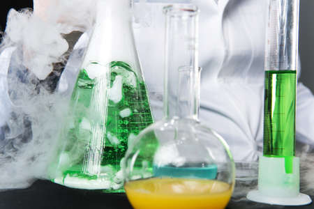 closeup on chemical studies in laboratory and flasks. man sitting at table with tubes and flask with...
