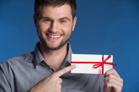 Present gift in hands of smiling man. closeup on happy man standing on blue background and pointingの写真素材