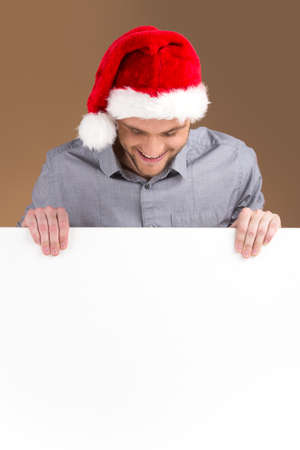 young man looking down on blank panel isolated on brown background. Smiling male looking down and wearing red hatの写真素材