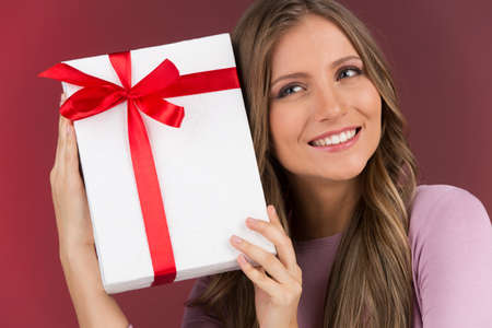 Gorgeous cute young woman holding present box. brunette girl holding present close and thinkingの写真素材
