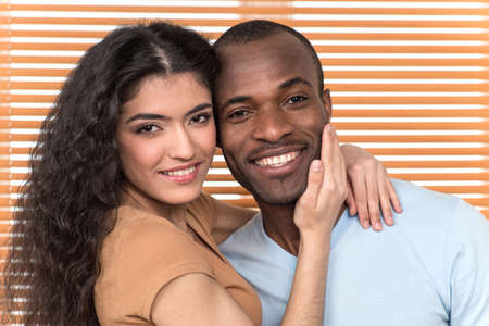 pretty couple hugging and looking into camera. African man and Hispanic woman standing close before shuttersの写真素材
