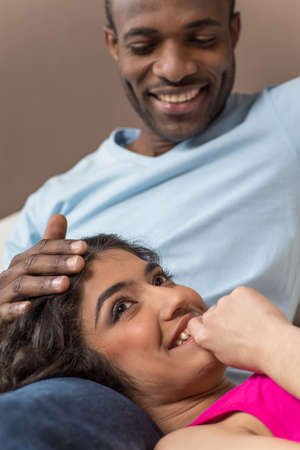 Closeup on happy African American woman lying on man legs. Couple in their thirties sitting at home together laughing.の写真素材
