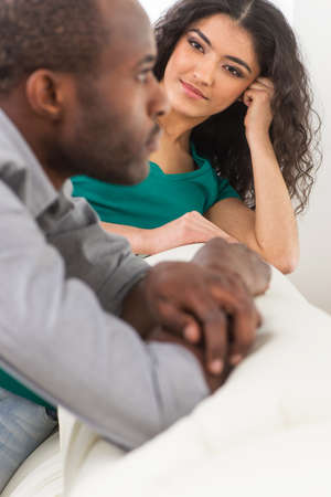 Couple in living room talking while sitting on sofa. profile of black african man sitting on sofa and looking awayの写真素材
