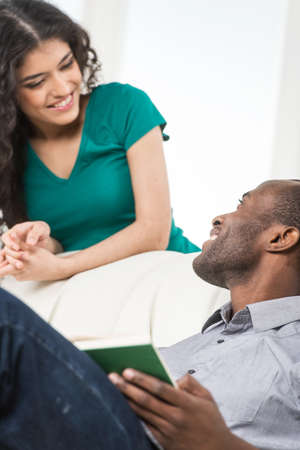 Couple in living room talking while sitting on sofa. profile of black african man sitting on sofa and looking at womanの写真素材