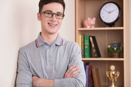 portrait of handsome young man smiling indoor. guy wearing glasses looking into camera with bookshelves on backgroundの写真素材